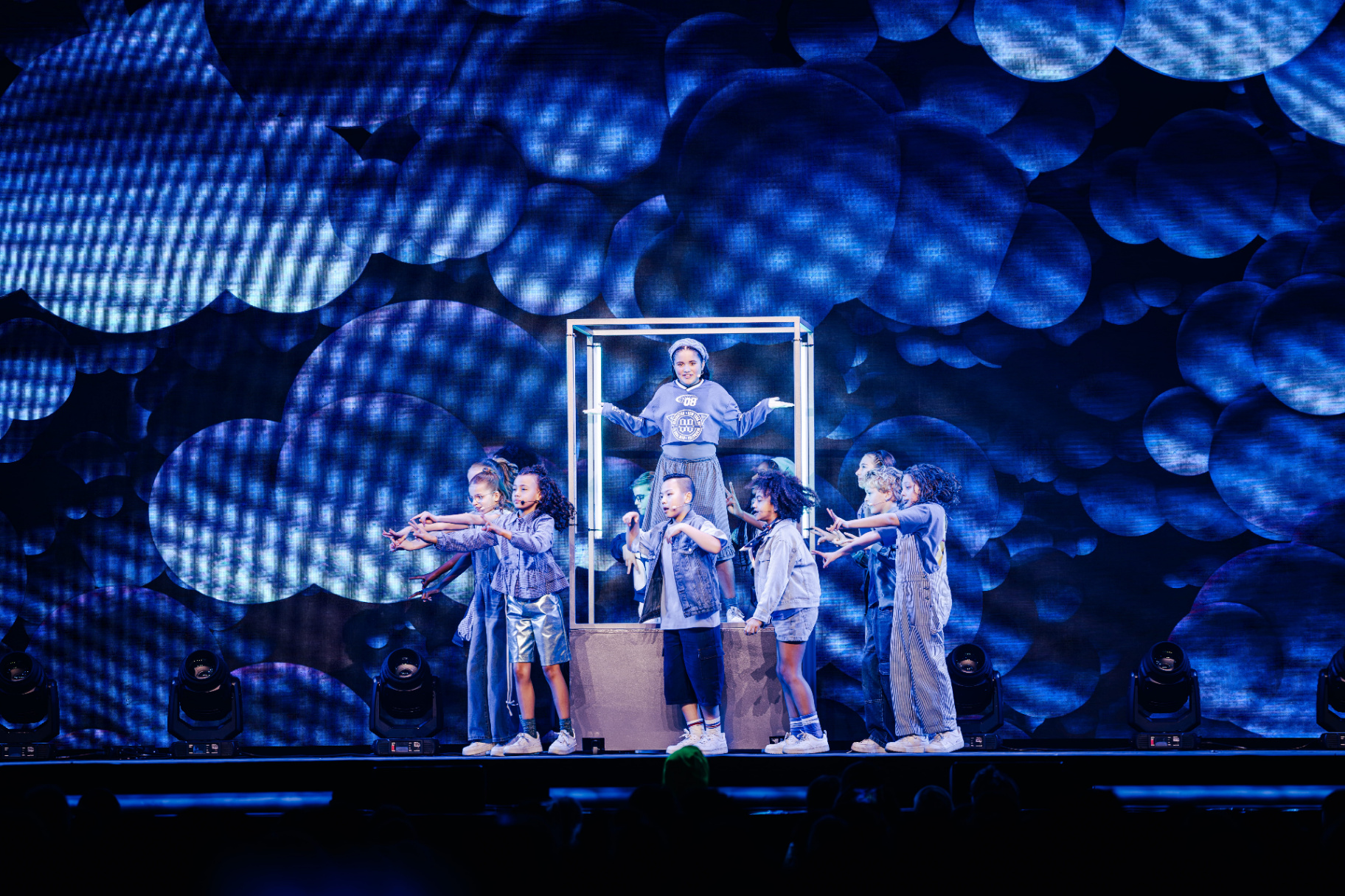 Marisa op podium in glazen kooi met dansers eromheen
