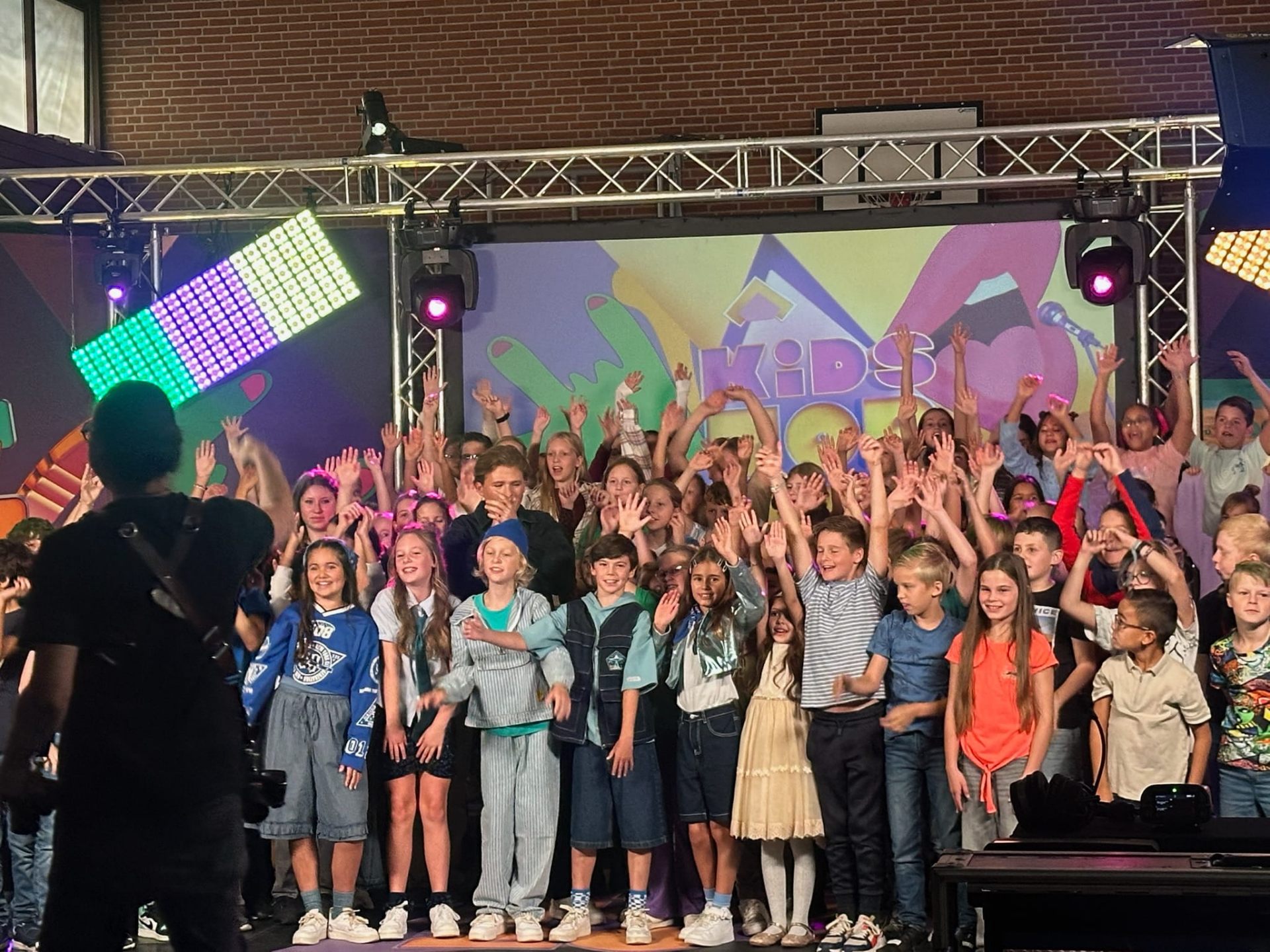 Volle zaal kinderen met handen in de lucht tijdens Kids Top