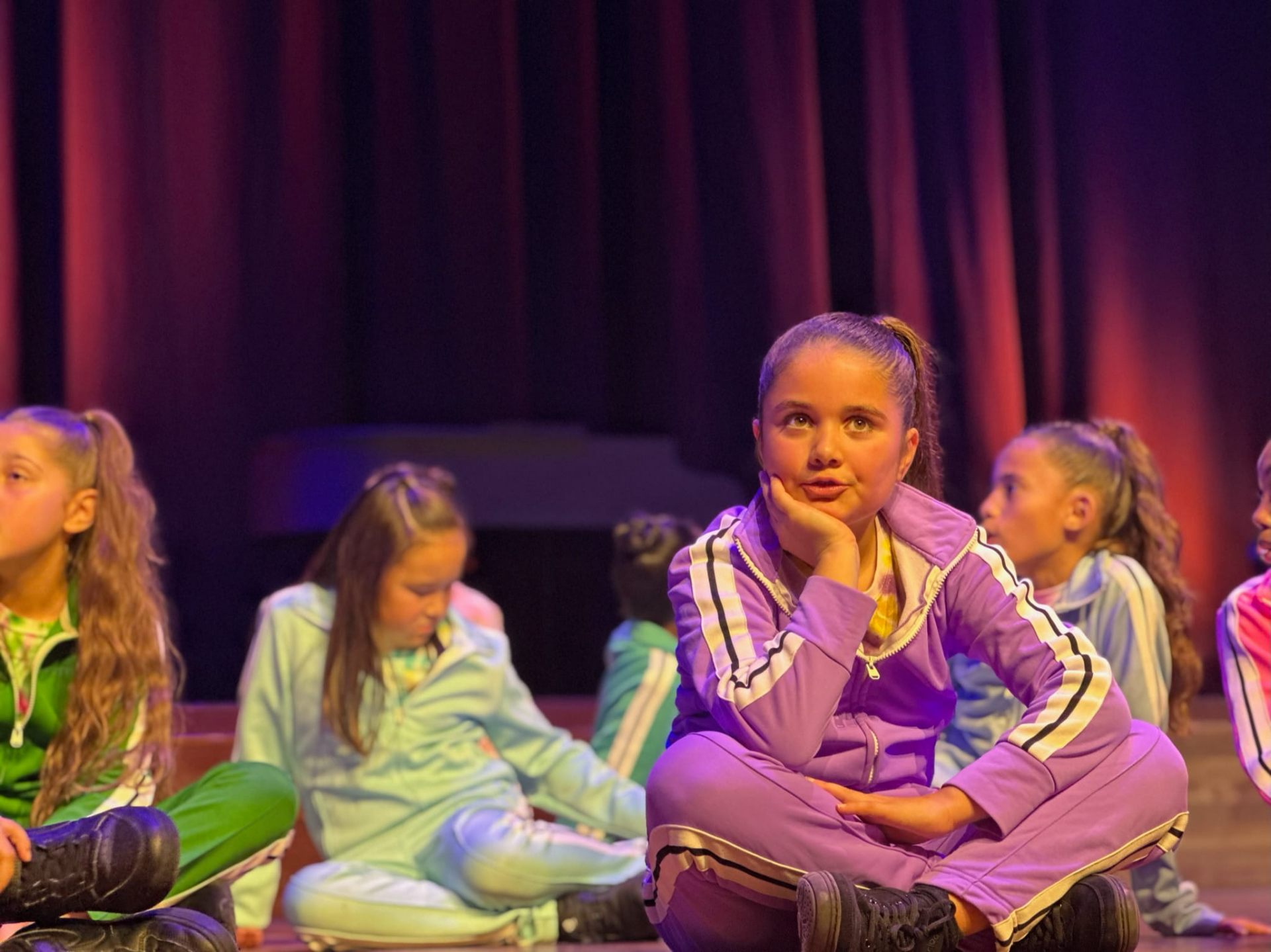 Marisa zit in paars trainingspak op het podium tussen het koor