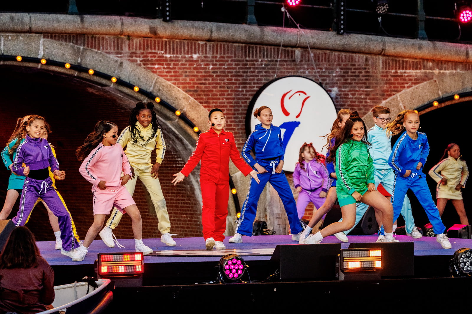 Kinderen voor Kinderen koor in kleurrijke trainingspakken op de gracht